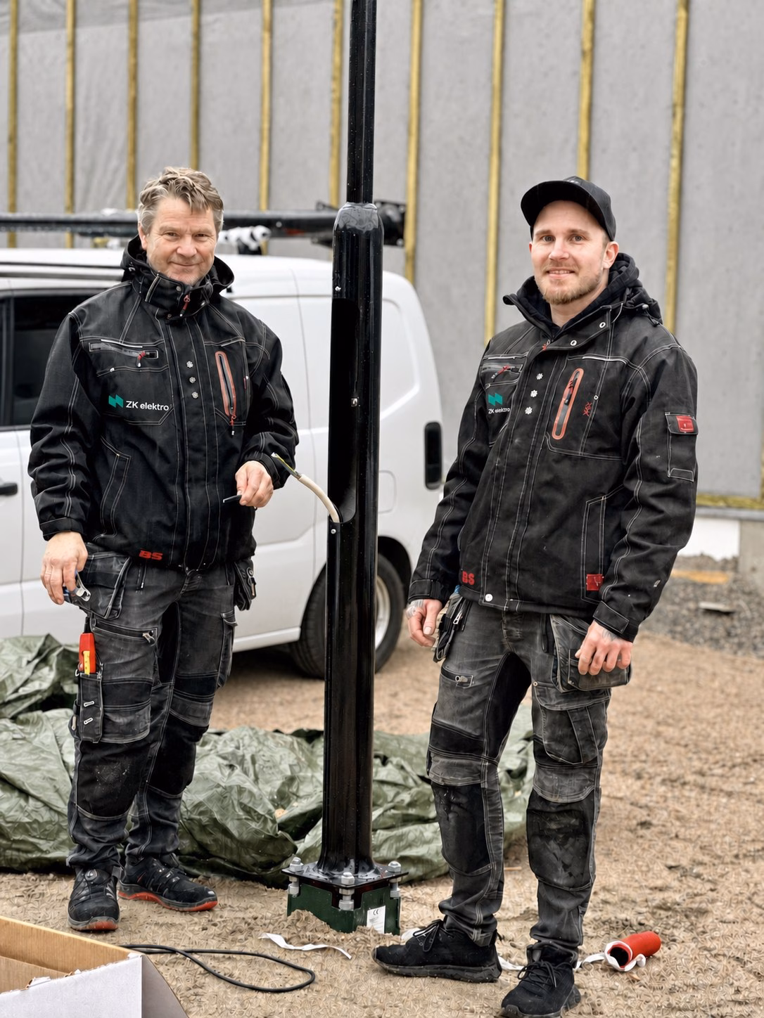 To montører i ZK Elektro-arbeidstøy ved en lysstolpe under montering