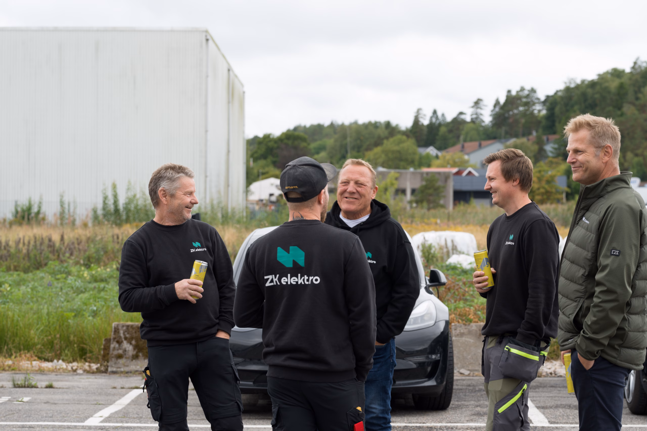 En gruppe kollegaer i samtale utendørs, flere med ZK Elektro på arbeidstøyet.