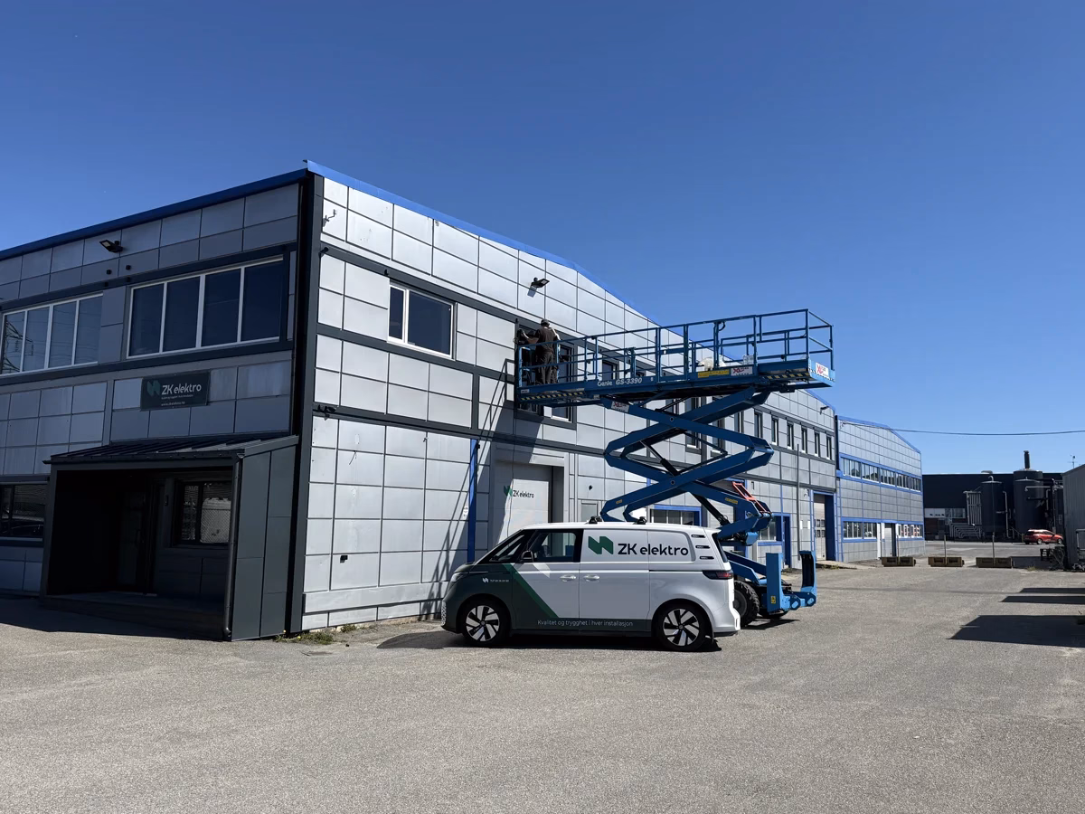 ZK Elektros kontorbygg og firmabil, med en montør i lift ved fasaden.